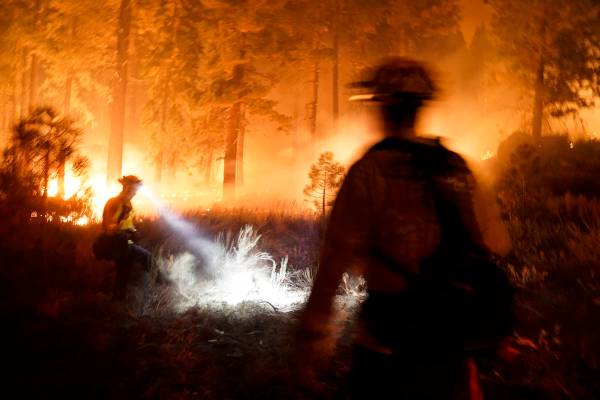 Dos bomberos crean un corte de combustible mientras el “Caldor Fire" arde cerca de las casas ...