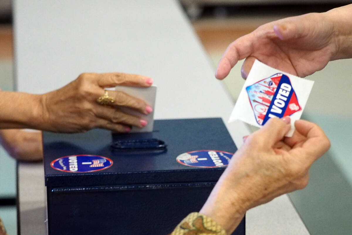 Un trabajador electoral entrega a un votante una calcomanía que muestra que votó mientras otr ...