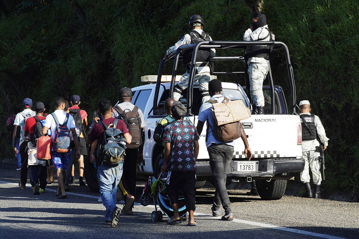 Migrantes, en su mayoría de Centroamérica, pasan junto a la Guardia Nacional mientras caminan ...