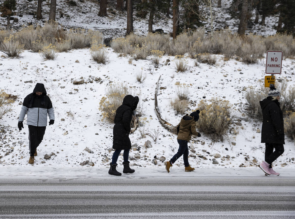 Gente camina a lo largo de la carretera cubierta de nieve mientras cae una ligera nevada en el ...