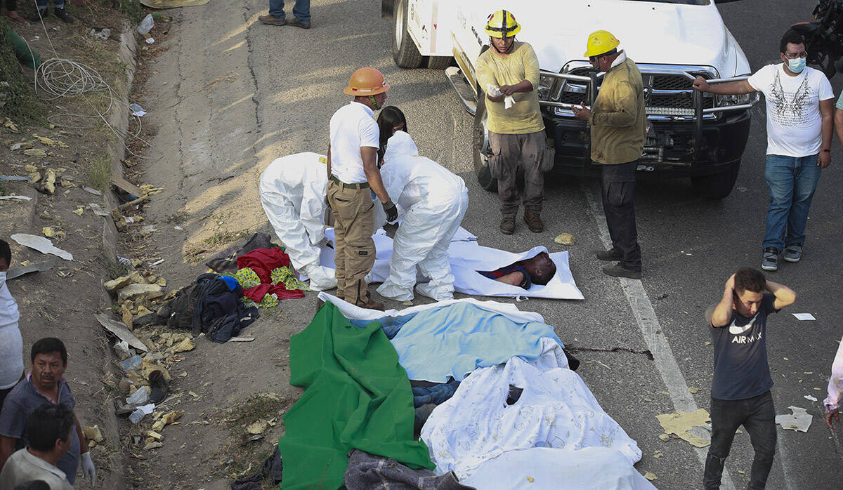 Los cuerpos en bolsas para cadáveres se colocan a un costado de la carretera después de un ac ...