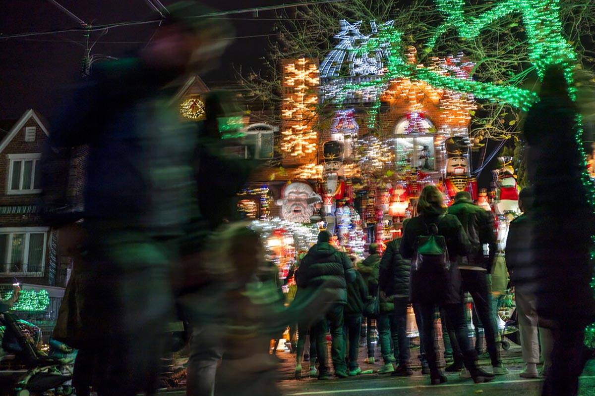 La gente se agolpa alrededor de las luces y decoraciones navideñas que adornan una casa en el ...