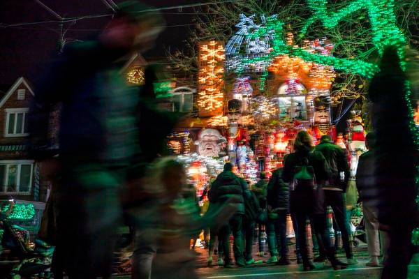 La gente se agolpa alrededor de las luces y decoraciones navideñas que adornan una casa en el ...