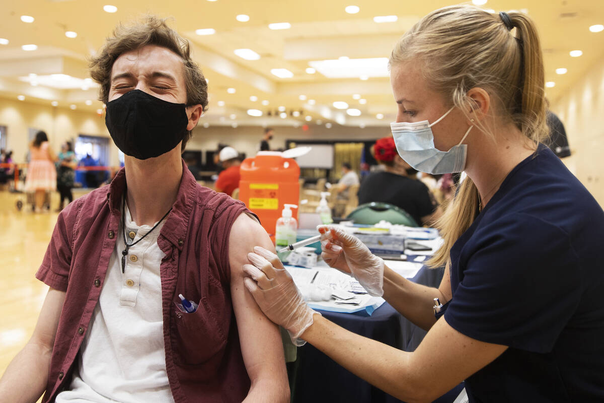Jared Fessler, a la izquierda, recibe su vacuna contra COVID-19 de la estudiante de asistencia ...