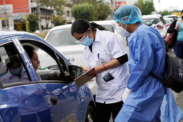 Trabajadores de farmacia recopilan información mientras la gente hace fila en sus autos para l ...