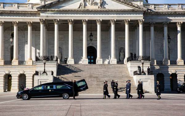 Un coche fúnebre que lleva el féretro envuelto en la bandera estadounidense del ex senador de ...