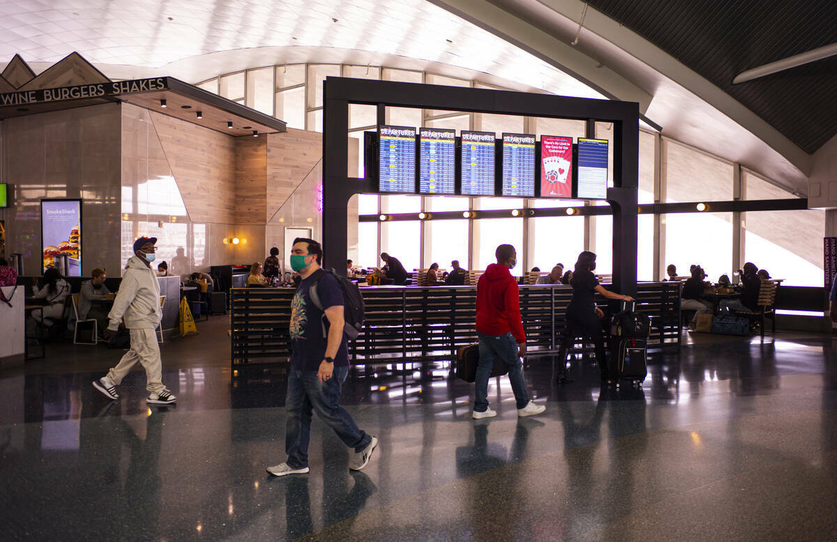 Viajeros caminan junto a una pantalla que enlista las salidas en la Terminal 1 del Aeropuerto I ...