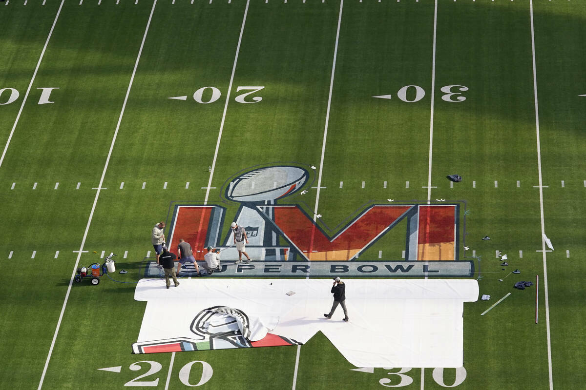 Los trabajadores pintan un logotipo en el campo del SoFi Stadium mientras los miembros de los m ...