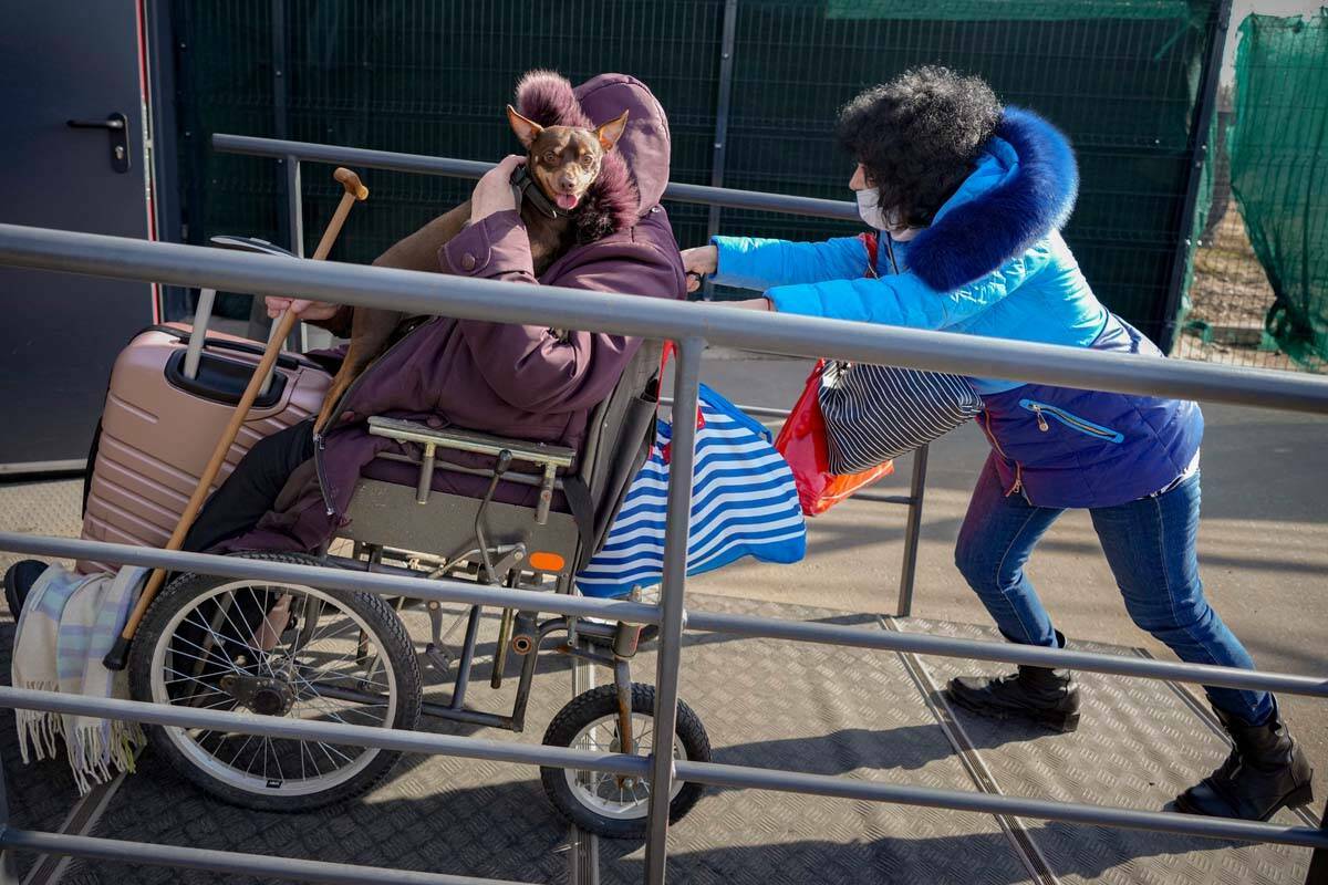 Una mujer empuja una silla de ruedas que transporta a una anciana con un perro desde el territo ...