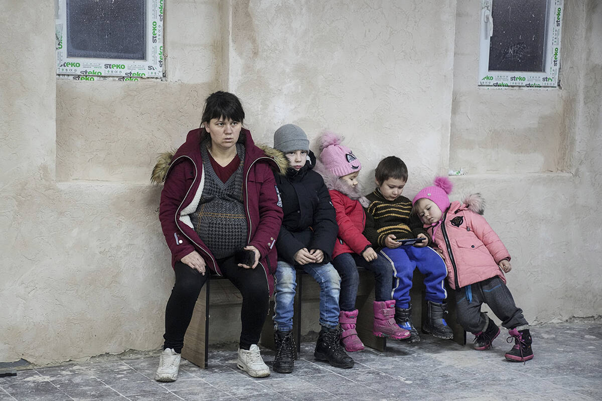Una mujer embarazada y sus niños se sientan en un banco, en el refugio antibombas improvisado ...