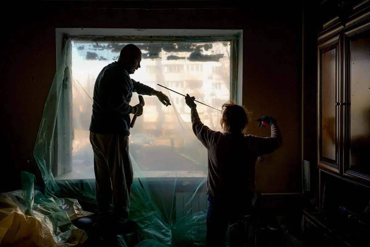 Slava Chikov, a la izquierda, cubre con una lámina de plástico la ventana destrozada de su sa ...