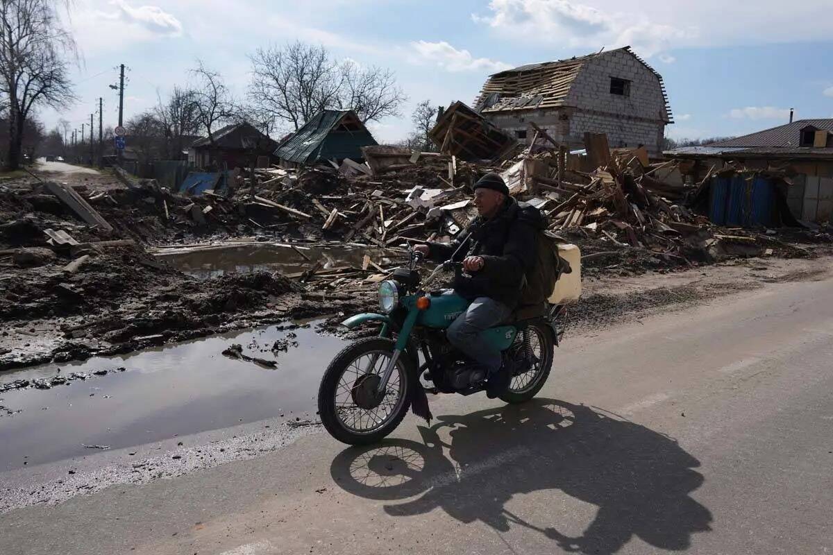 Un hombre pasa en moto por delante de una casa dañada por los bombardeos en Chernihiv, Ucrania ...