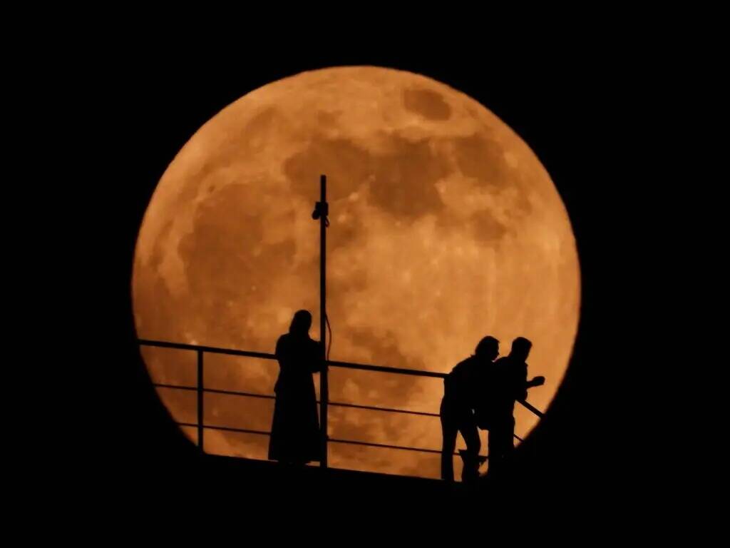 La gente se siluetea mientras una luna casi llena se eleva sobre el cielo en Grozny, Rusia, el ...