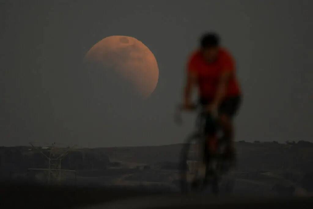 Un eclipse lunar se ve detrás de un ciclista durante la primera luna de sangre del año, en Ir ...