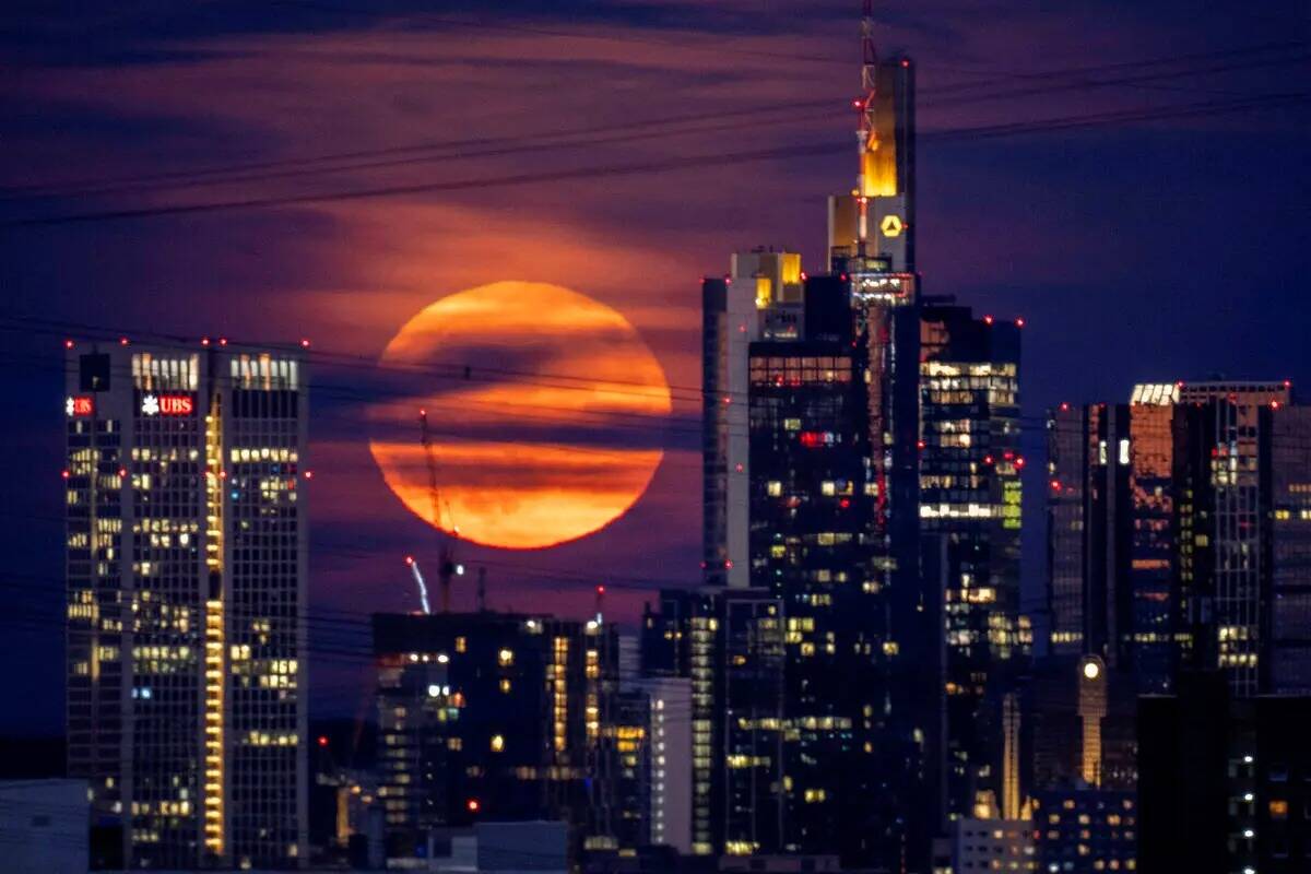 La luna llena se eleva detrás de los edificios en el distrito bancario de Frankfurt, Alemania, ...