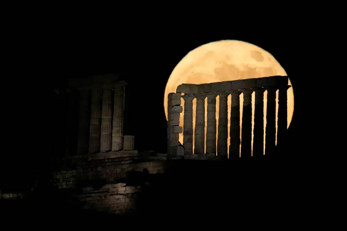 La luna llena de fresa se eleva detrás del antiguo templo de Poseidón en el Cabo Sounion, a u ...