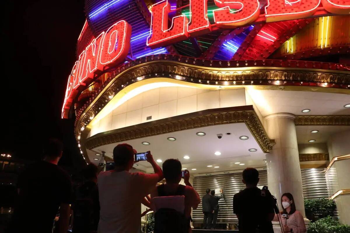 La gente toma fotos mientras la seguridad cierra las persianas del Casino Lisboaʡt a medianoch ...