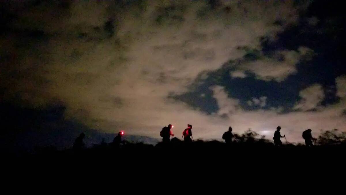 Excursionistas nocturnos de verano silueteados a lo largo de un sendero en el Área de Conserva ...