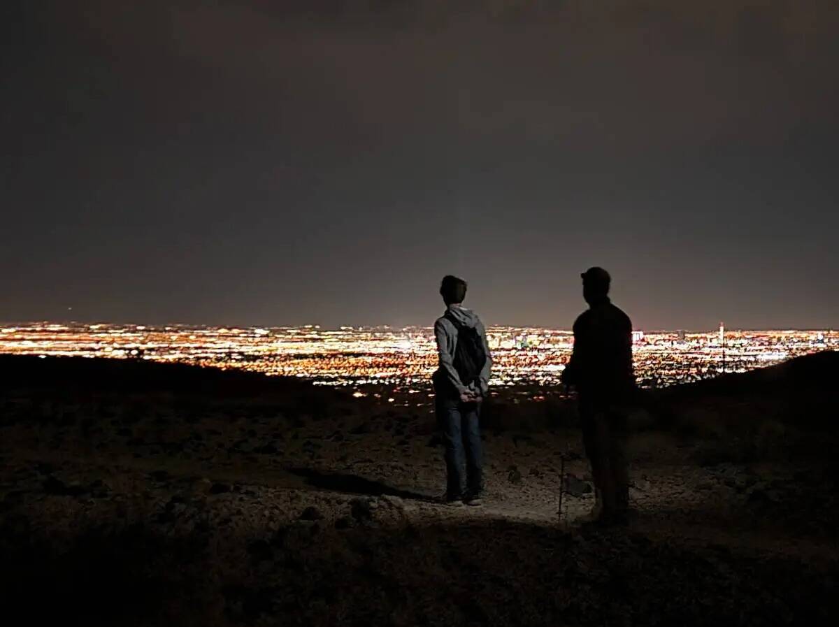 Excursionistas nocturnos disfrutan de una vista de las brillantes luces de Las Vegas desde un s ...