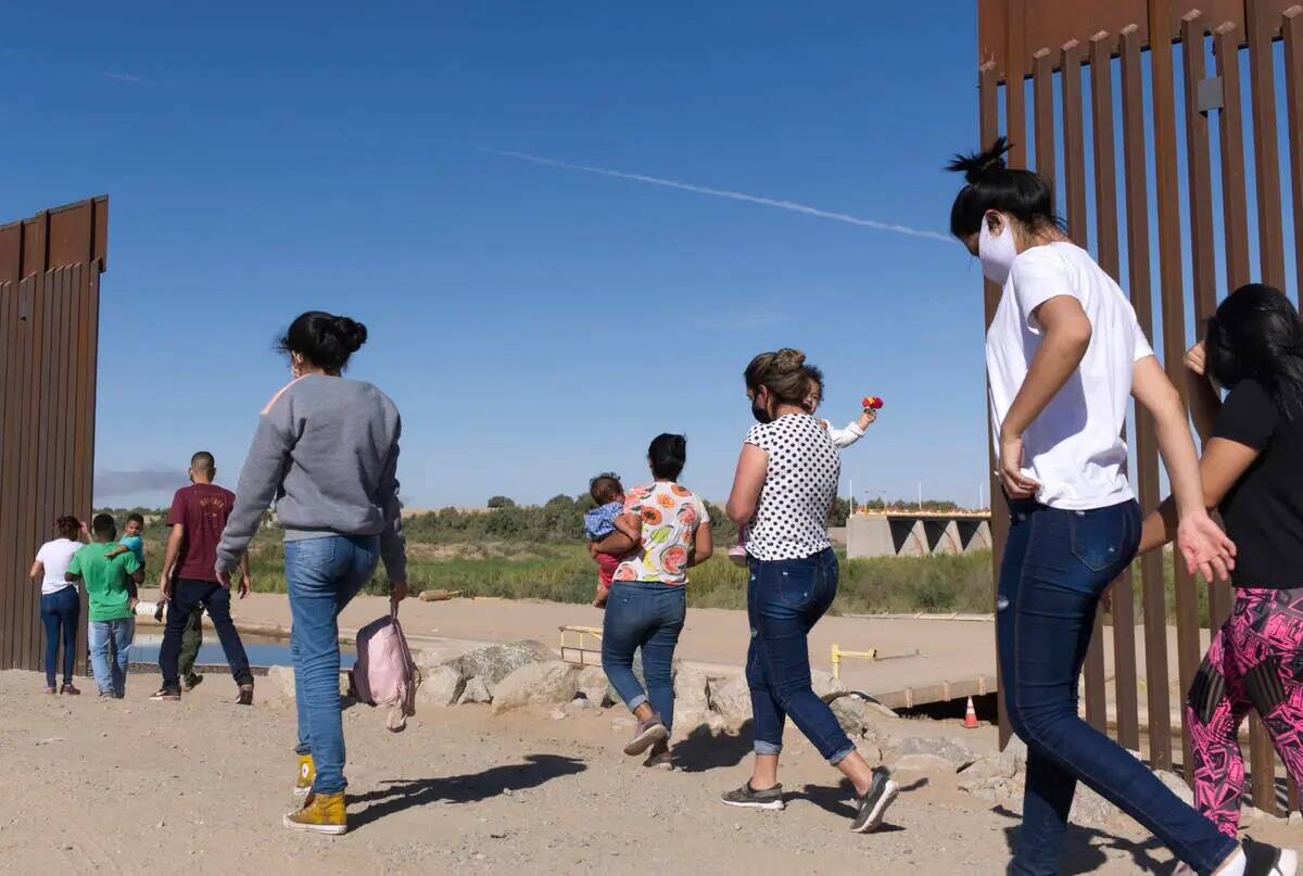 ARCHIVO - Un grupo de migrantes brasileños se abre paso por una brecha en la frontera entre Es ...