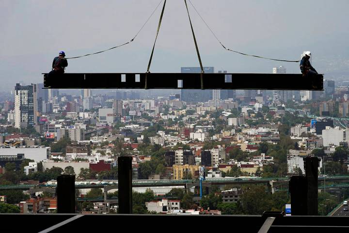 ARCHIVO.- Trabajadores de la construcción están sobre una viga colgada de una grúa en un edi ...