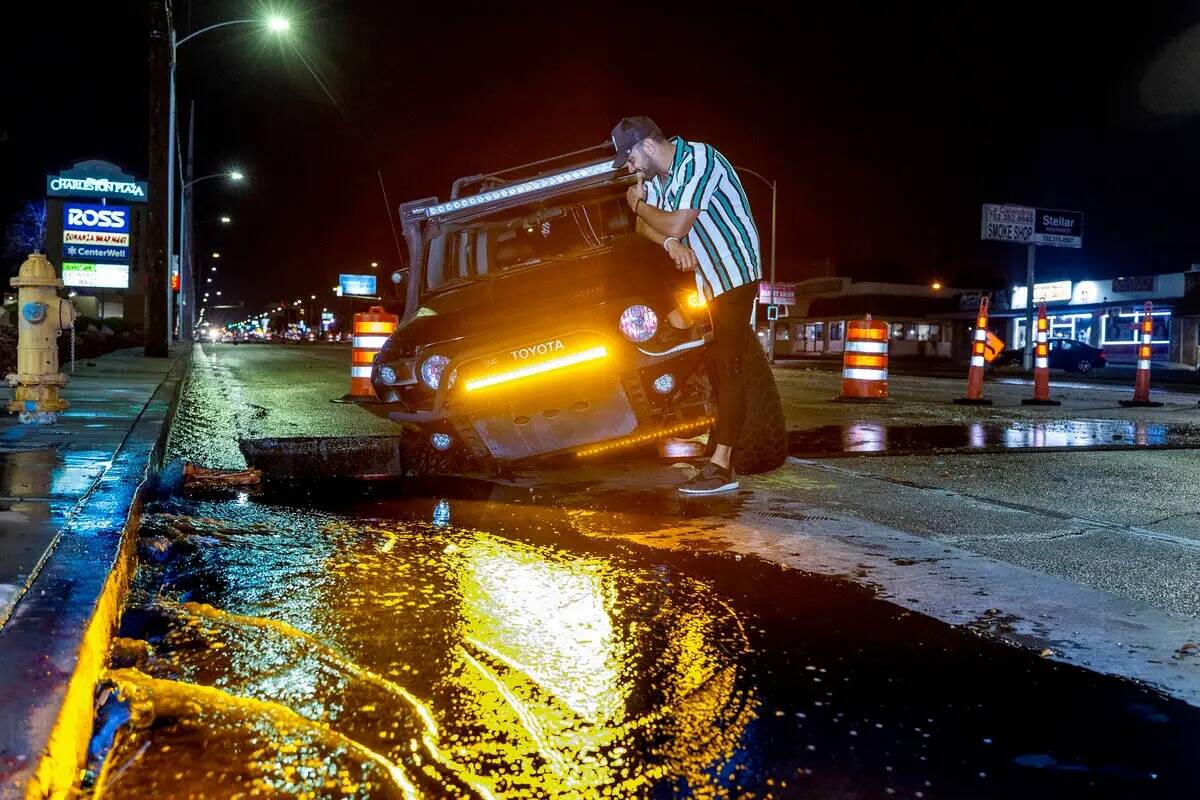 El conductor Miguel Reyes revisa su auto atascado en un agujero de construcción debido a la in ...