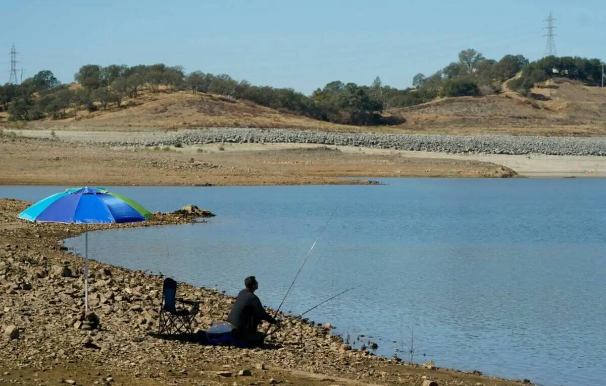 Un hombre coloca su caña de pescar a lo largo de la línea de la orilla de Folsom Lake que nor ...
