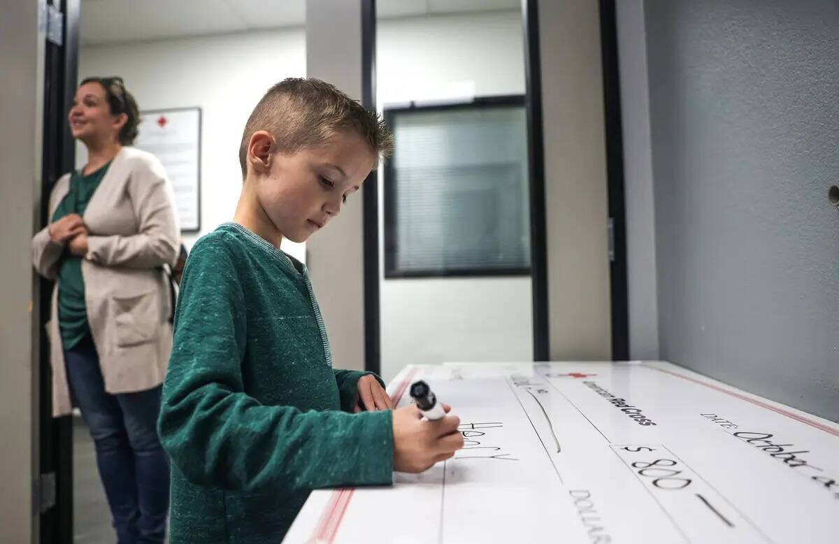 Henry Williams, de seis años, firma un cheque de 800 dólares para la Cruz Roja Americana en l ...