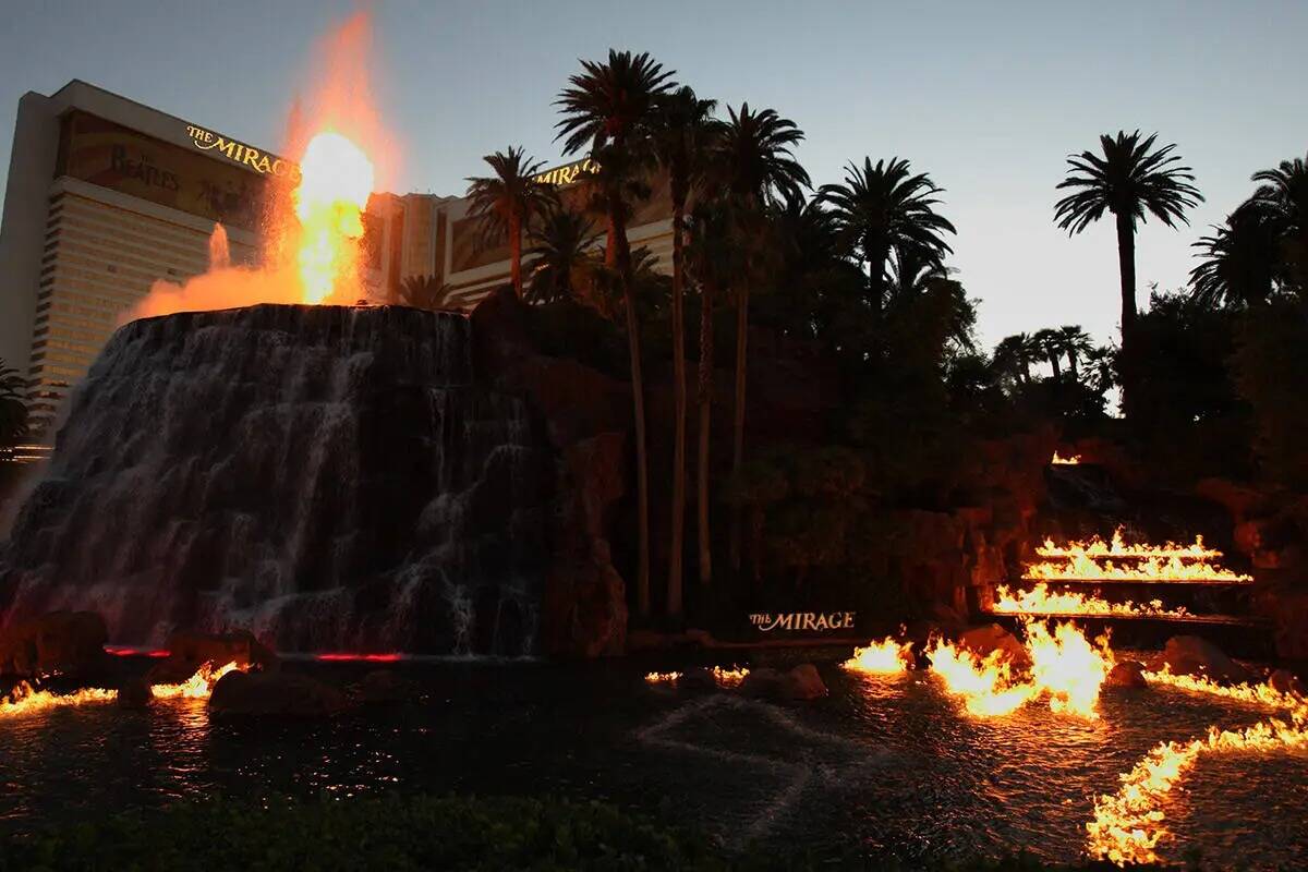 El volcán arroja fuego mientras las llamas bailan sobre la superficie del agua frente al hotel ...
