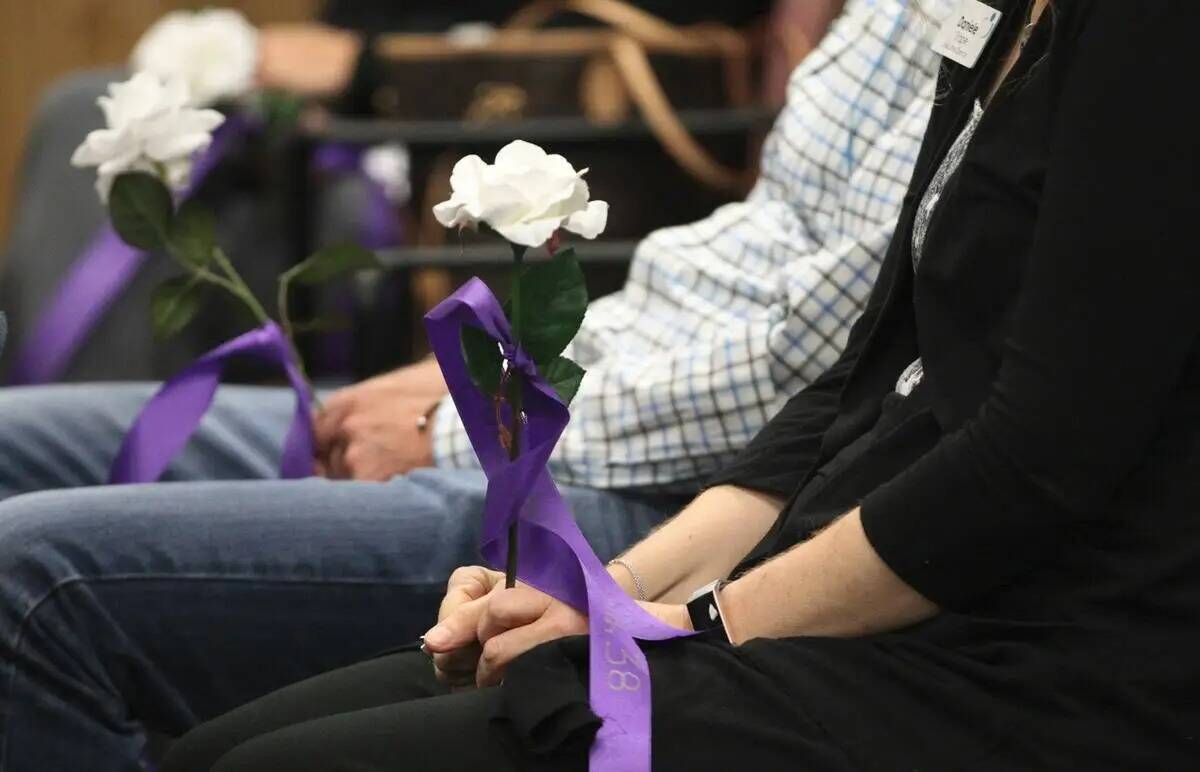 Un grupo de personas sostiene flores con los nombres de las víctimas de violencia doméstica a ...