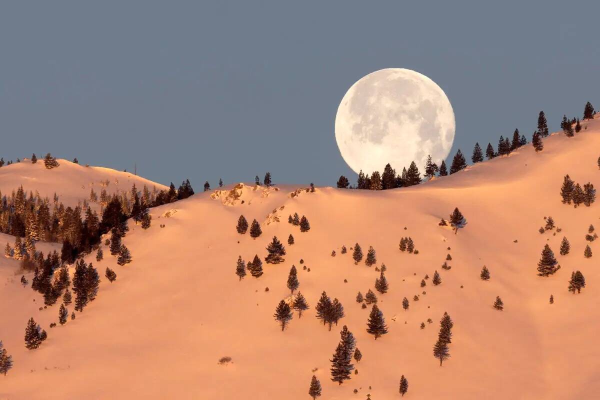 La Luna de Nieve de febrero se pone detrás de las montañas cubiertas de nieve el lunes 6 de f ...