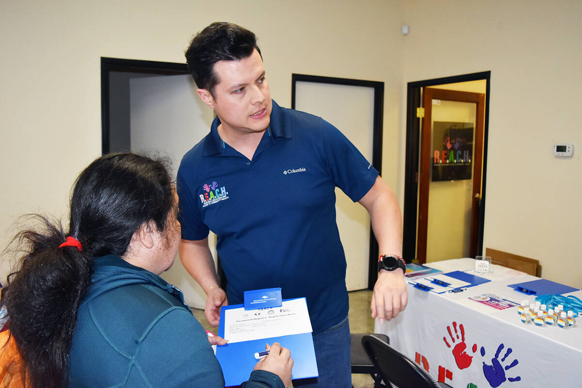 Óscar Aceves, director de Alcance Comunitario de R.E.A.C.H. informa a una asistente a la Feria ...
