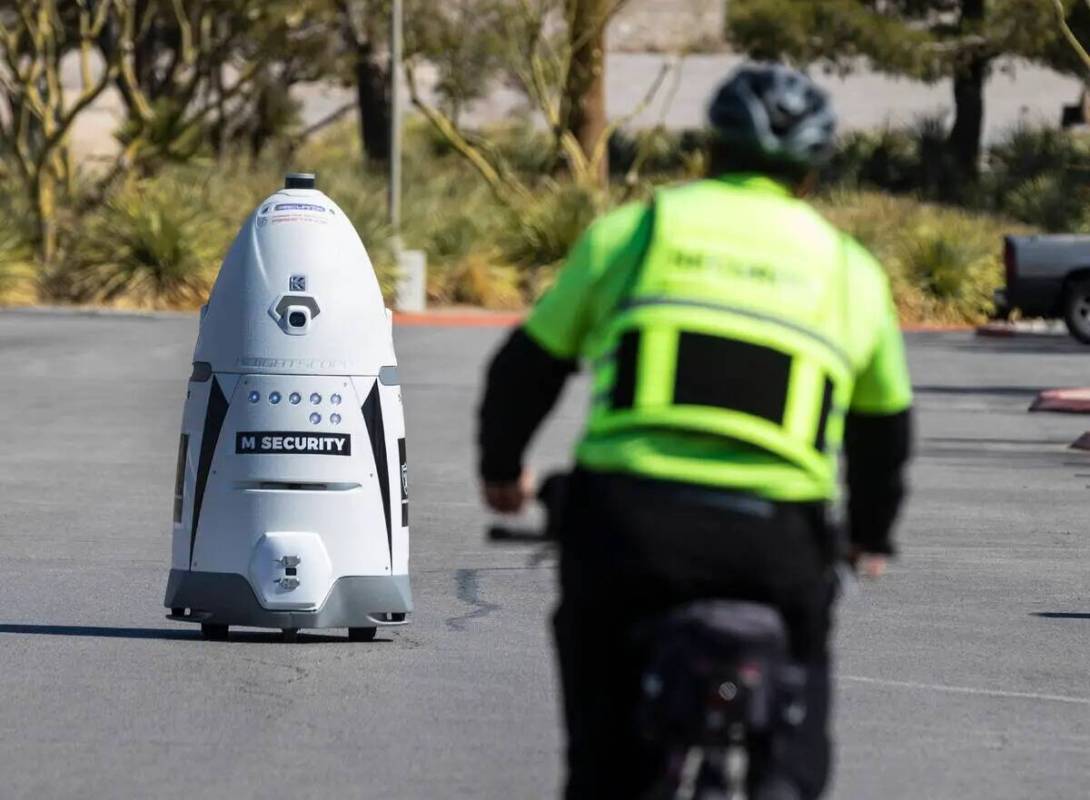 Un guardia de seguridad de M Resort conduce su bicicleta hacia el robot autónomo de tamaño hu ...