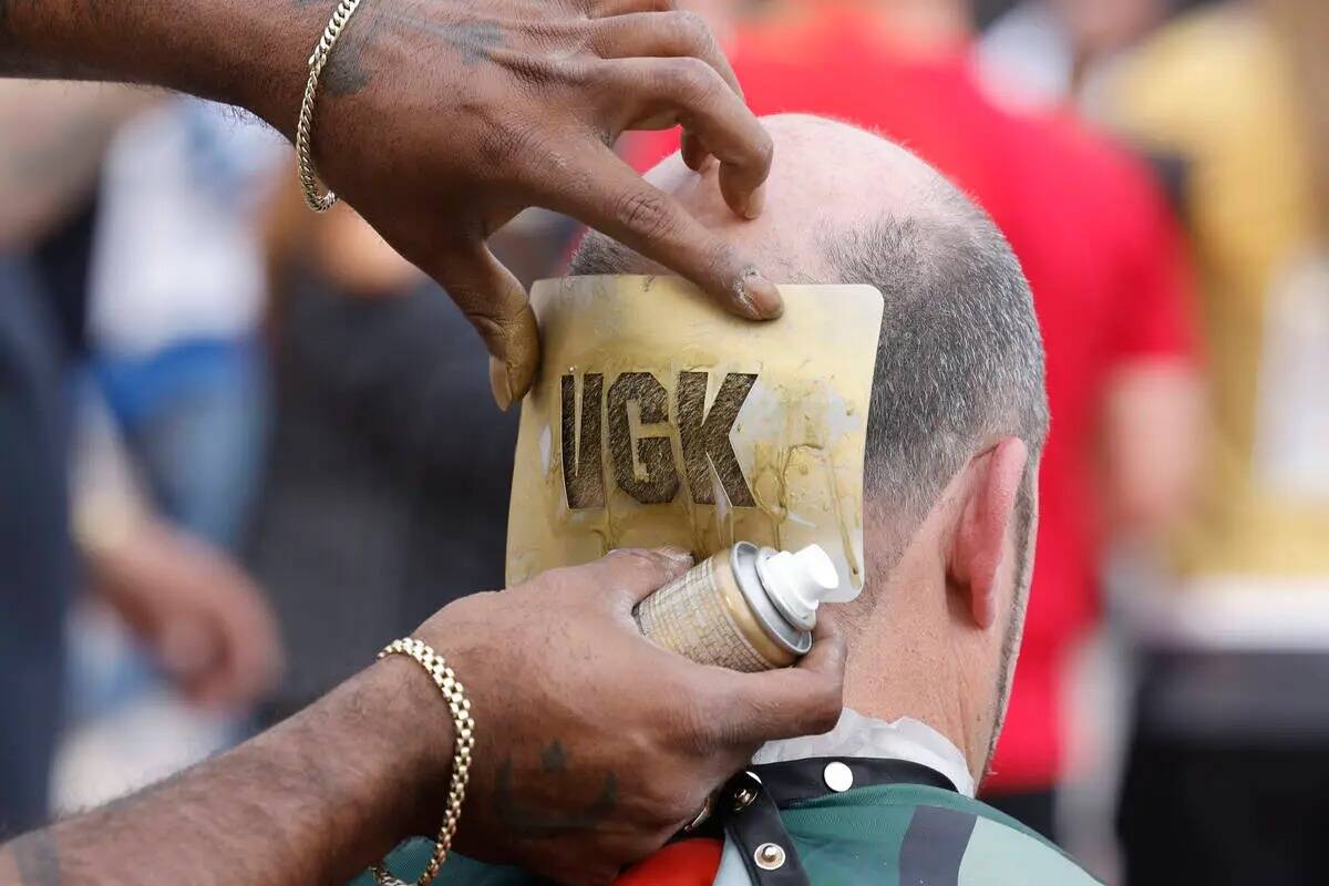 Garrett Thomas de 101 Barbershop usa spray dorado para pintar las letras "VGK" para su cliente ...