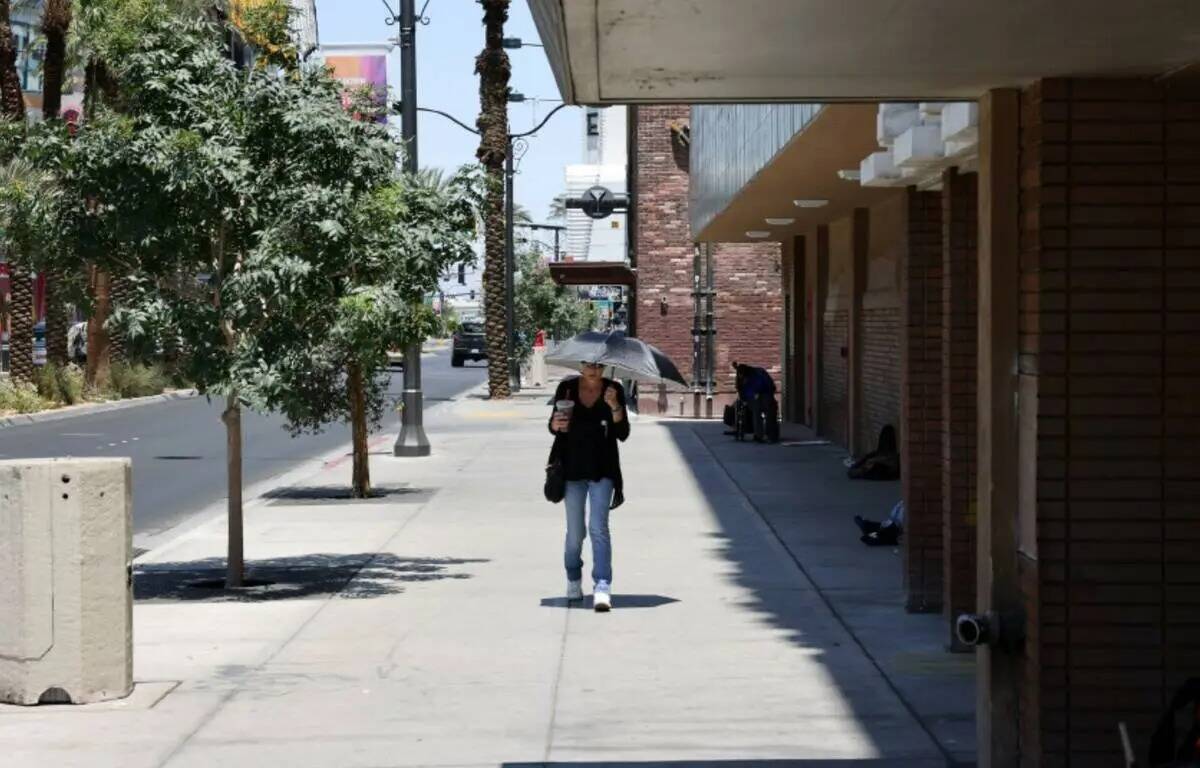 Un visitante hace frente al calor con un paraguas y una bebida helada en Las Vegas Boulevard a ...