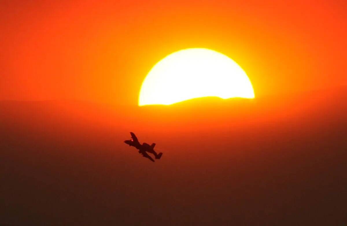Un A-10 de la Fuerza Aérea se ve volando por el sol parcialmente oscurecido por el humo del in ...