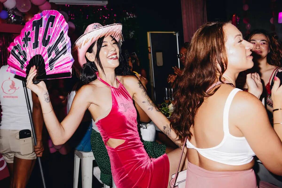 Una mujer lleva un sombrero de vaquera rosa y usa un fan durante un brunch drag show temático ...