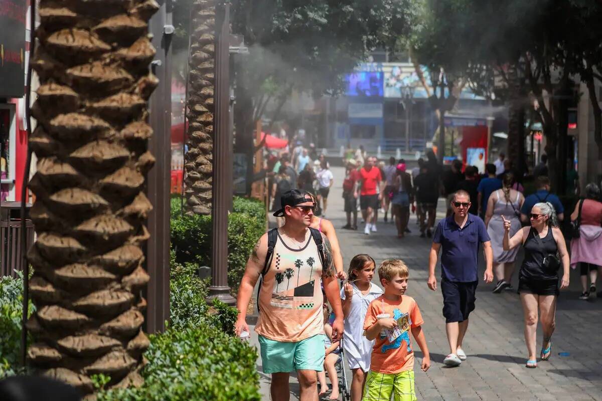 La gente desafía el calor a lo largo del Strip caminando a través de una fila de rociadores e ...