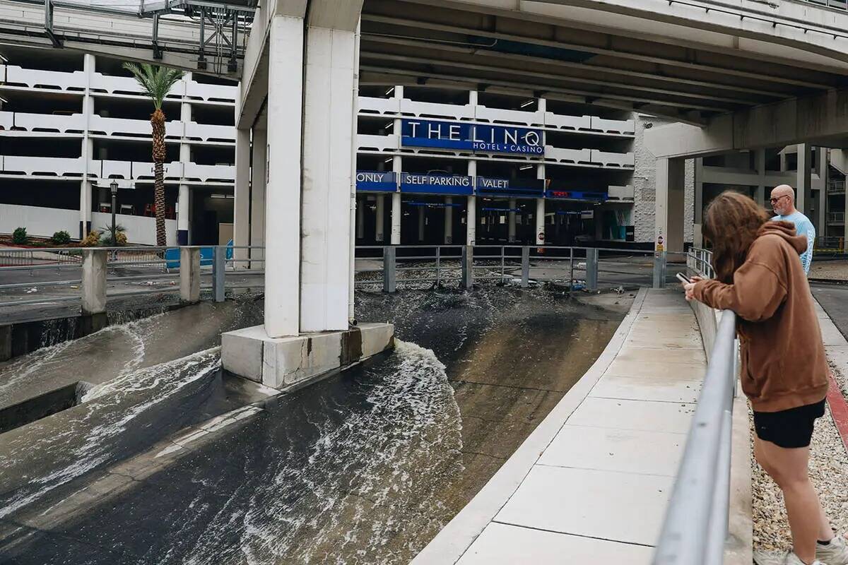 Varias personas observan cómo el agua fluye hacia un canal de inundación desde el estacionami ...