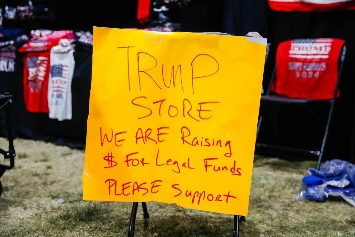 Un cartel se encuentra al final de una mesa de mercancías de Trump en ReAwaken America Tour el ...