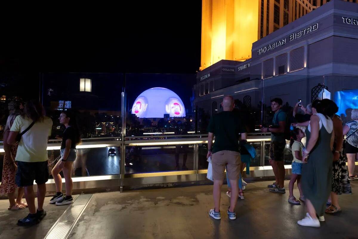 Visitantes del Strip de Las Vegas observan The Sphere en el puente peatonal sobre Sands Avenue ...