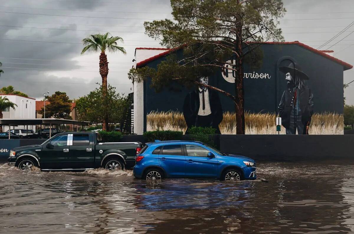 Autos circulan a través Inundaciones repentinas se derraman sobre la acera y en un estacionami ...