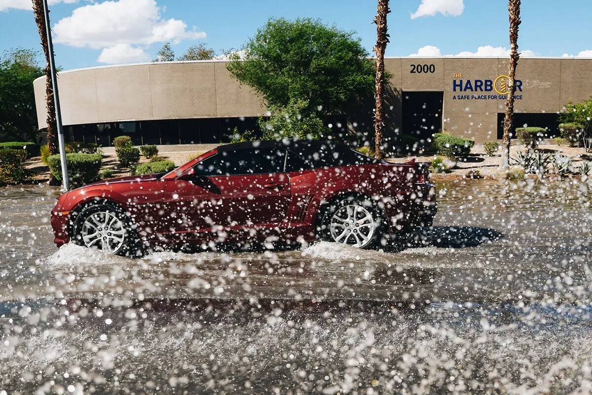 Un auto conduce a través de la inundación residual de las recientes lluvias en North Mojave R ...