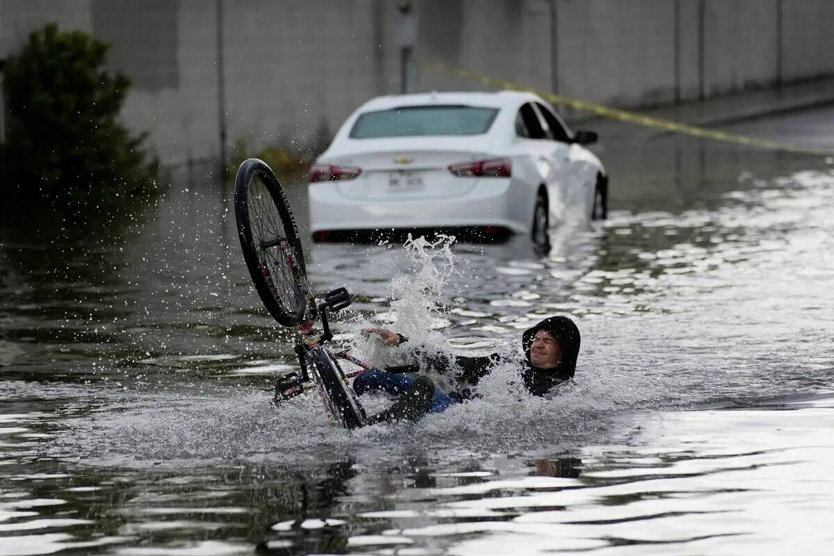 Un ciclista se cae mientras intenta atravesar las aguas cerca de un auto varado en una calle in ...