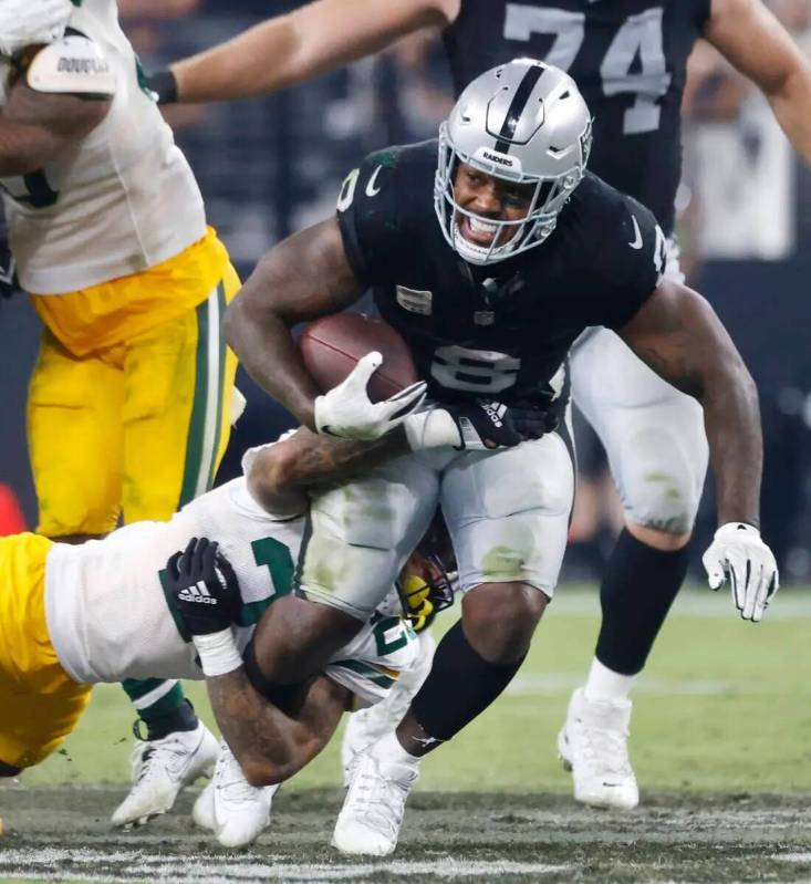 El running back de los Raiders Josh Jacobs (8) rompe las tacleadas del safety de los Green Bay ...