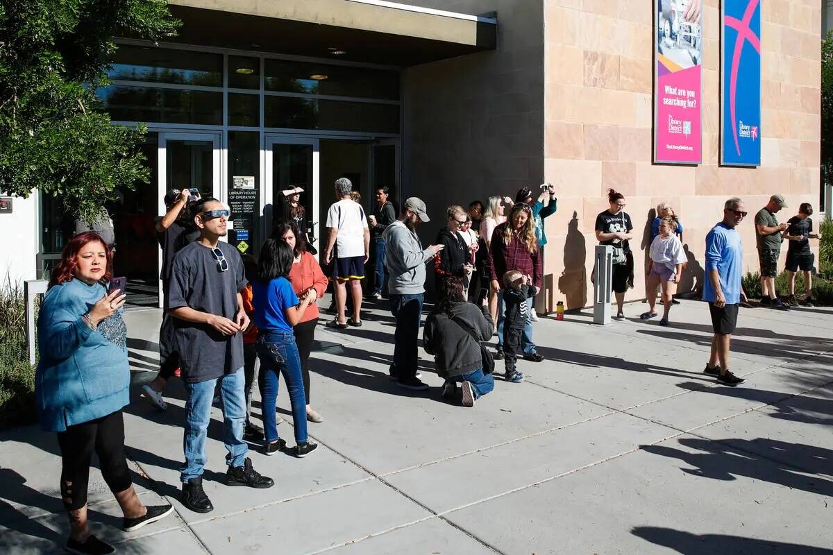Un grupo de personas observa el eclipse solar anular desde Centennial Hills Library mientras pa ...