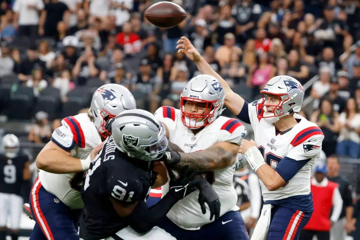 El quarterback de los New England Patriots Mac Jones (10) lanza bajo la presión de la defensiv ...