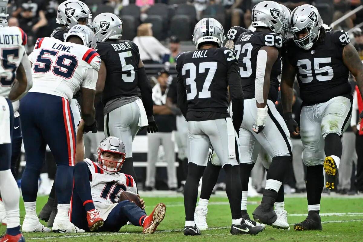 El quarterback de los New England Patriots, Mac Jones, abajo a la izquierda, es ayudado a levan ...