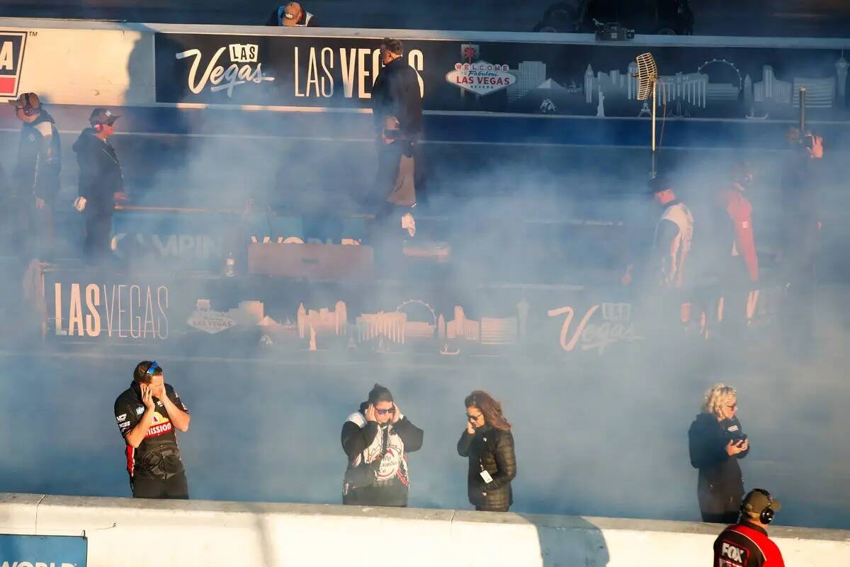 El equipo de pits y los espectadores se abren paso entre el humo del burnout en el NHRA Nevada ...