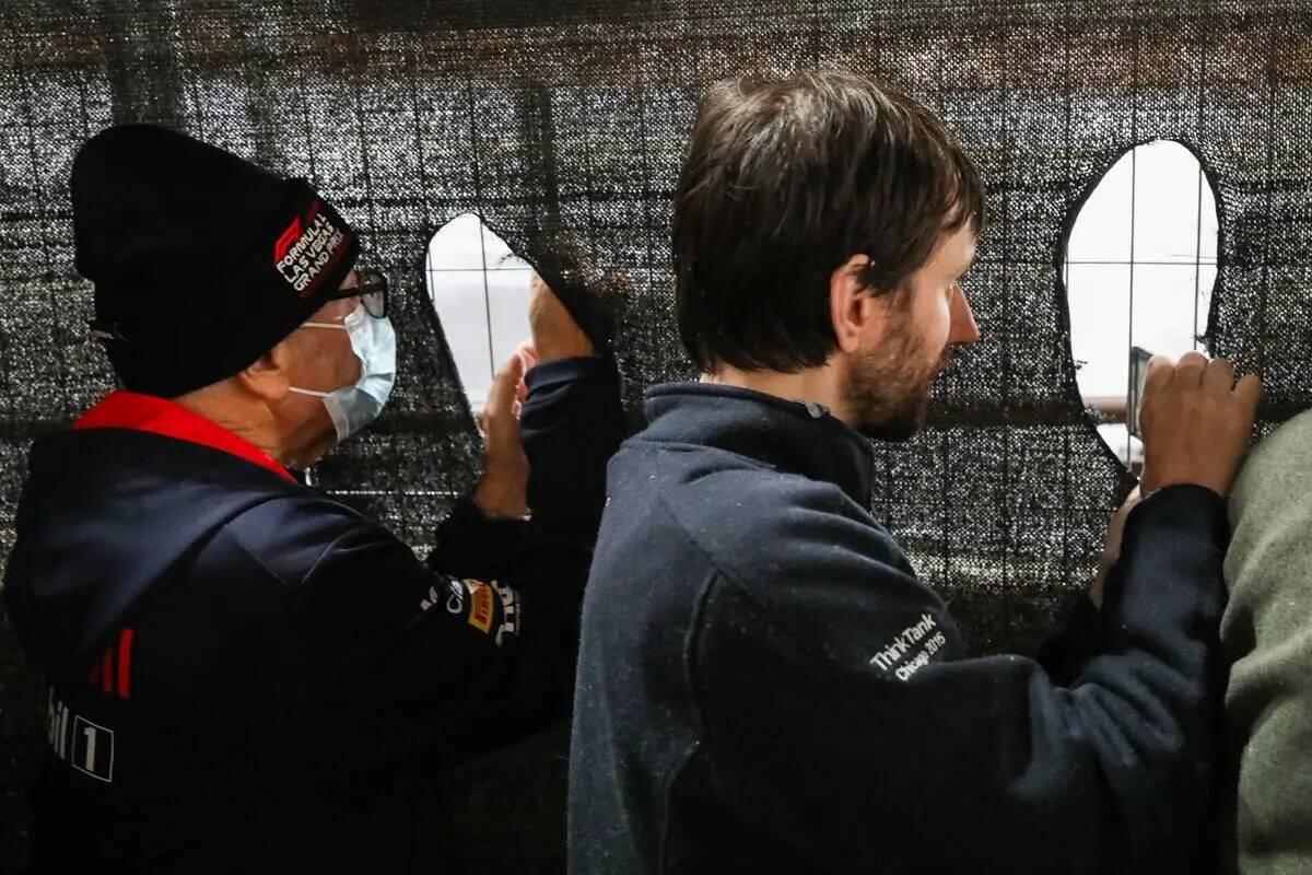 Unos fans hacen agujeros en una valla para ver la carrera final del Grand Prix de Las Vegas de ...